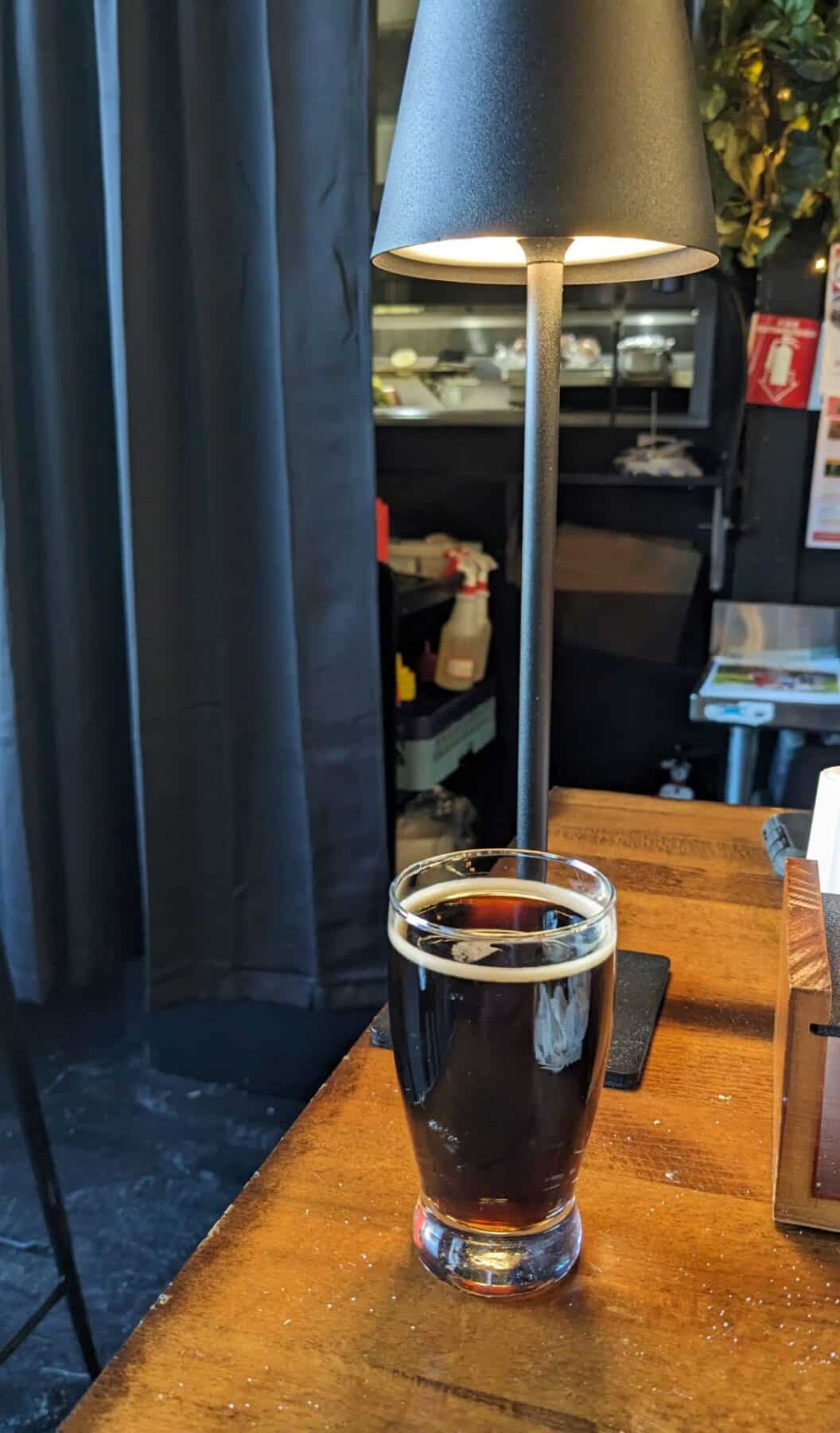 A short pour of dark beer under a light on a table.